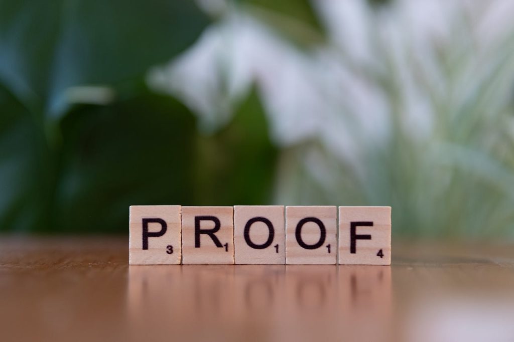 scrabble-tiles-spelling-the-word-proof-30901572 Wooden Scrabble tiles spelling PROOF on a wooden table with green background.