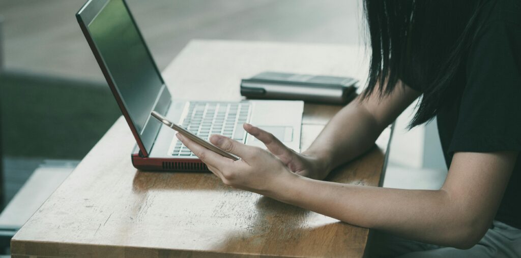 pexels-photo-363766-363766 A young woman multitasking with her smartphone and laptop at a table indoors.